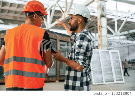 Builder is talking with manager or architect. Two workers are in the industrial wooden warehouse 133218904