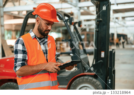 Forklift is behind, digital tablet in hands. Industrial worker in wooden warehouse 133218964