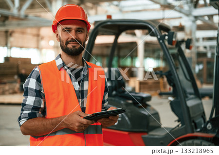 Forklift is behind, digital tablet in hands. Industrial worker in wooden warehouse 133218965