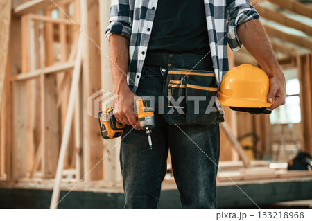 Orange colored drill and hardhat in hands. Industrial worker in wooden warehouse 133218968