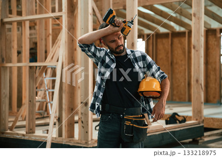 Building the house, holding hard hat and drill. Industrial worker in wooden warehouse 133218975
