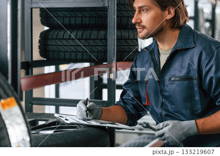 Writing the data into notepad. Man is in the tire fitting car service 133219607