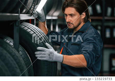 Strong worker is with tire. Man is in the tire fitting car service Strong worker is with tire. Man is in the tire fitting car service 133219733