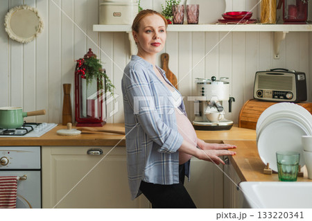 Pregnancy motherhood people expectation future. Pregnant woman with big belly smiling in kitchen at home. Girl hugging her tummy enjoying pregnancy. Maternity tenderness parenthood new life concept Pregnancy motherhood people expectation future. Pregnant woman with big belly smiling in kitchen at home. Girl hugging her tummy enjoying pregnancy. Maternity tenderness parenthood new life concept 133220341