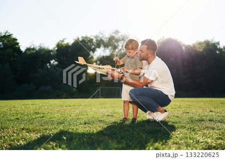 Kid is learning how to fix it by screwdriver. Father and son are on the field together with toy plane 133220625