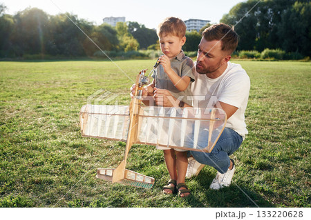 Screwdriver in hand, fixing it. Father and son are on the field together with toy plane 133220628