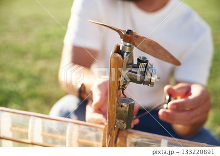 Made of wood. Man is on the field fixing the toy plane Made of wood. Man is on the field fixing the toy plane 133220891