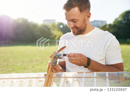 Man is on the field fixing the toy plane 133220897
