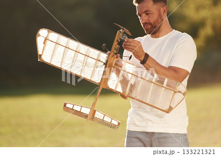 In casual clothes. Man is on the field fixing the toy plane 133221321