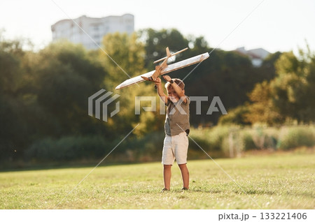 Up in the air, holding it. Cute little boy is playing with toy plane on the field 133221406