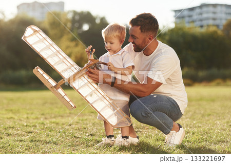 Kid is learning how to fix it by screwdriver. Father and son are on the field together with toy plane 133221697