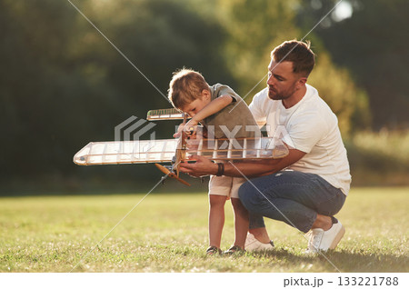 Trying to fix it with screwdriver. Father and son are on the field together with toy plane 133221788