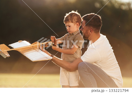 Illuminated by sunlight, fixing broken toy. Father and son are on the field together with plane Illuminated by sunlight, fixing broken toy. Father and son are on the field together with plane 133221794