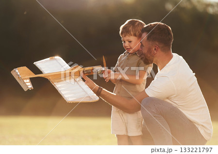 Illuminated by sunlight, fixing broken toy. Father and son are on the field together with plane Illuminated by sunlight, fixing broken toy. Father and son are on the field together with plane 133221797