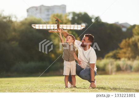 Happy facial expression, fun. Father and son are on the field together with toy plane 133221801