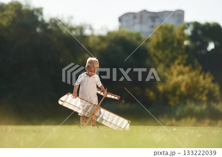 Holding it in hands. Cute little boy is playing with toy plane on the field 133222039