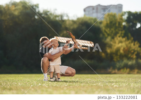 Sitting together. Father and son are on the field with toy plane Sitting together. Father and son are on the field with toy plane 133222081