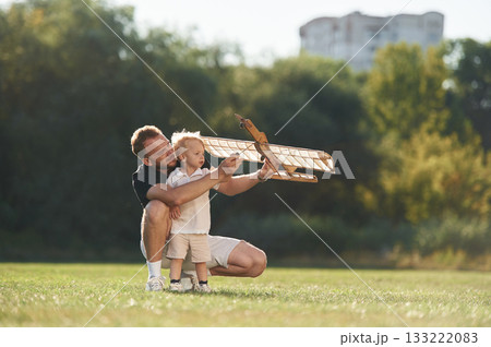 Screwdriver in hand, fixing it. Father and son are on the field together with toy plane Screwdriver in hand, fixing it. Father and son are on the field together with toy plane 133222083
