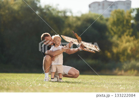 Screwdriver in hand, fixing it. Father and son are on the field together with toy plane Screwdriver in hand, fixing it. Father and son are on the field together with toy plane 133222084