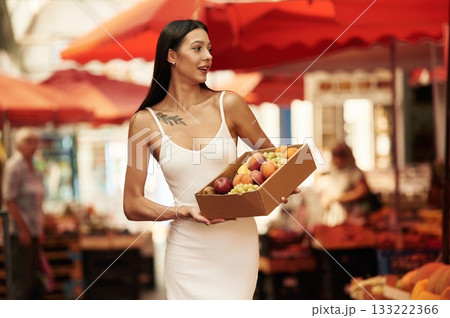 Grapes, peaches, and other fruits in a box. Young woman is on the vegetable market or bazaar Grapes, peaches, and other fruits in a box. Young woman is on the vegetable market or bazaar 133222366