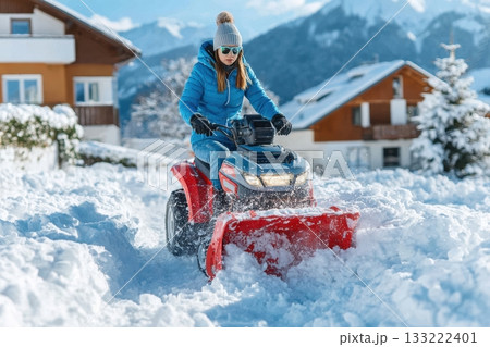 Woman using snow plow on quad bike clearing driveway in winter landscape 133222401