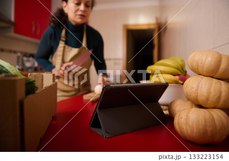 Woman In Apron Preparing Food In Kitchen With Tablet And Fresh Produce On Counter 133223154