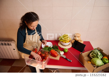 Woman Preparing Fresh Produce At Kitchen Counter With Tomatoes Bananas Greens And Boxed Veggies Woman Preparing Fresh Produce At Kitchen Counter With Tomatoes Bananas Greens And Boxed Veggies 133223162