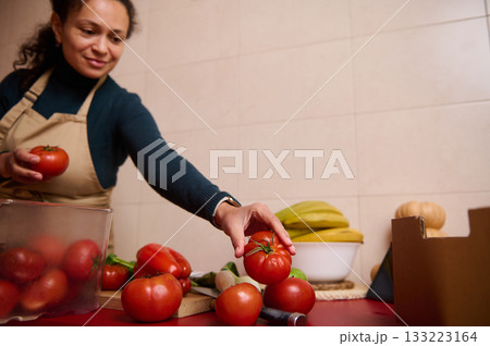 Woman In Apron Selecting Fresh Tomatoes In Kitchen For Cooking Or Market Prep 133223164