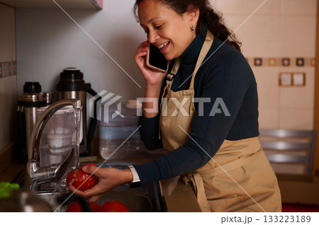 Busy Woman In Apron Washing Tomatoes At Kitchen Sink While Talking On Phone Busy Woman In Apron Washing Tomatoes At Kitchen Sink While Talking On Phone 133223189