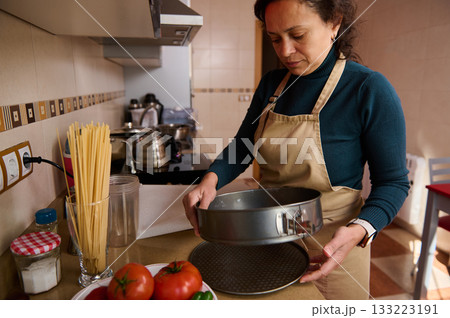 Home Cook in Apron Preparing Pan, Fresh Tomatoes, and Spaghetti in a Cozy Kitchen 133223191