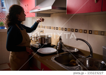Woman Cooking Pasta In Modern Kitchen With Pot On Stove And Strainer In Sink 133223227
