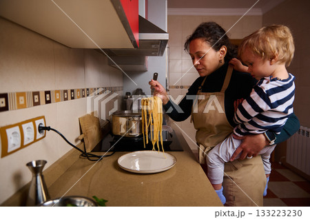 Mother Cooking Pasta With Child In Warm Kitchen, Sharing A Moment Of Bonding Mother Cooking Pasta With Child In Warm Kitchen, Sharing A Moment Of Bonding 133223230