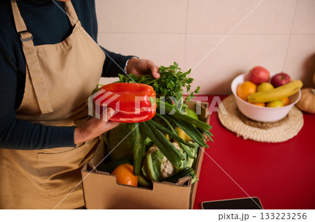 Person In Kitchen Apron Holding Red Pepper Over Box Of Fresh Produce 133223256