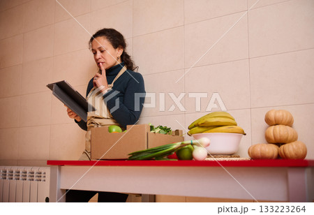 Woman In Apron Reviewing Tablet In A Kitchen With Produce And Pumpkins On Table 133223264