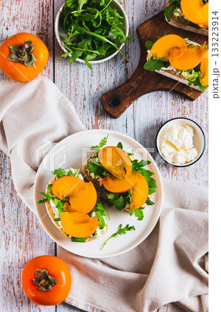 Persimmon, herbs and cream cheese on ciabatta on a plate on the table top and vertical view Persimmon, herbs and cream cheese on ciabatta on a plate on the table top and vertical view 133223914