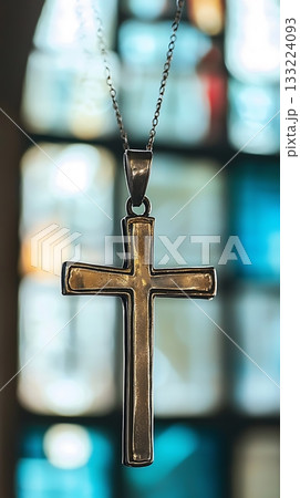 Silver cross necklace is hanging in front of a blue stained glass window 133224093