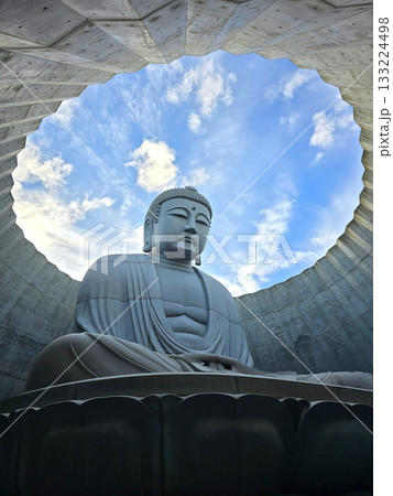 The serene Buddha statue is set against a backdrop of a bright blue sky, creating a sense of peace and tranquility 133224498