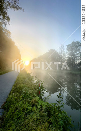 A stunning view of the morning mist gently hovering over calm water during a beautiful sunrise 133224832