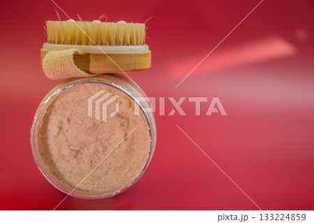 Skincare jar with creamy product and wooden brush on top, set against a bright red background, highlighting beauty and self-care routines Skincare jar with creamy product and wooden brush on top, set against a bright red background, highlighting beauty and self-care routines 133224859