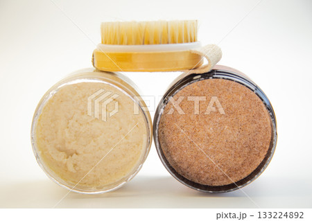 Two jars of body scrubs, one creamy and one coarse, paired with a wooden brush, highlighting natural skincare products for a refreshing and rejuvenating routine 133224892