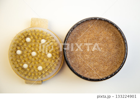 Round container of natural body scrub next to an exfoliating brush, highlighting organic skincare essentials for self-care and pampering experiences 133224901