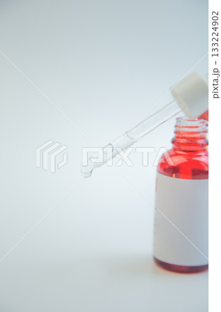 Dropper filled with vibrant red liquid hovers above a glass bottle, emphasizing skincare product design with a clean background, perfect for marketing and branding 133224902