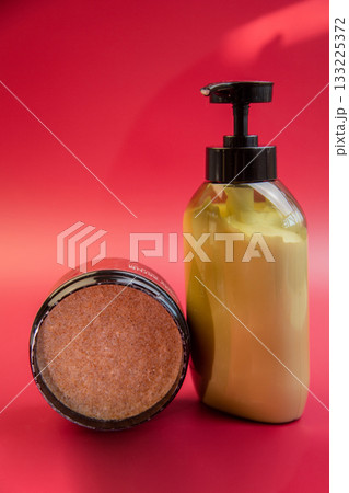Beauty products showcased on a bright red backdrop, including an exfoliating scrub jar and a moisturizing lotion pump bottle, ideal for skincare routines Beauty products showcased on a bright red backdrop, including an exfoliating scrub jar and a moisturizing lotion pump bottle, ideal for skincare routines 133225372