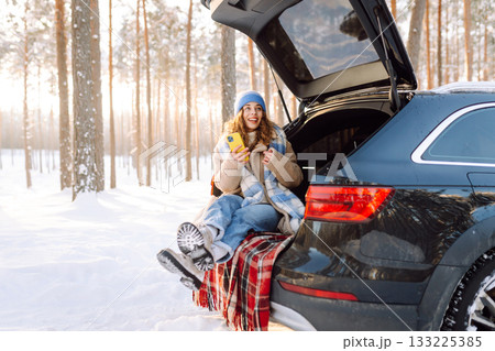 Happy Woman sitting in trunk, using phone. Snowy weather. Concept of adventure, travel by car. Happy Woman sitting in trunk, using phone. Snowy weather. Concept of adventure, travel by car. 133225385
