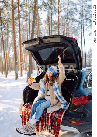 Selfie time. Young Woman sitting in trunk of car and taking selfie in winter forest. Rest, blogging. 133225522