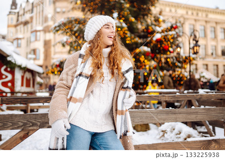 Smiling woman in a scarf and hat is having fun at a street holiday fair. Christmas concept. Smiling woman in a scarf and hat is having fun at a street holiday fair. Christmas concept. 133225938
