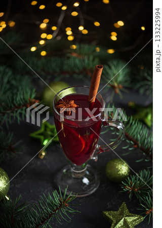Glass of Mulled Wine with Cinnamon Surrounded by Christmas Decor and Lights 133225994