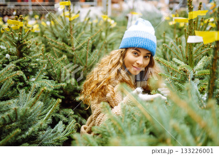 Young woman buys Christmas tree at fair. She chooses beautiful Christmas tree for her home interior. Young woman buys Christmas tree at fair. She chooses beautiful Christmas tree for her home interior. 133226001