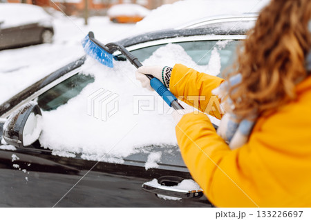 Woman cleaning snow off car during winter snowfall with brush. Scraping ice. Winter cleaning car. Woman cleaning snow off car during winter snowfall with brush. Scraping ice. Winter cleaning car. 133226697