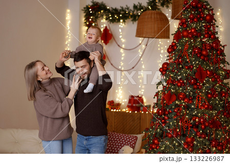 Happy family with baby celebrating Christmas in cozy living room with white wall 133226987